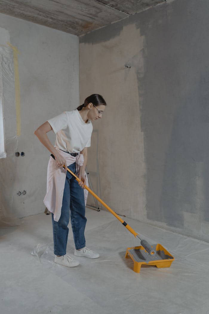 A woman uses a paint roller to apply gray paint on a wall during a home renovation project indoors.
